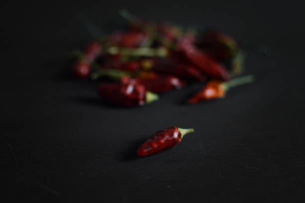 isolated red hot chili pepper with peppers behind in soft defocus. black background. low key