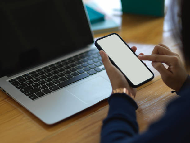 istock Female hands using smartphone while working with laptop on wooden table 1296298334