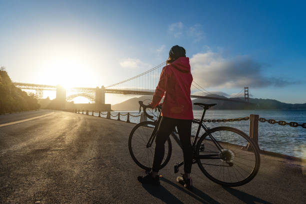 summer vacations in california: woman with bicycle by the golden gate bridge - bridge road city golden gate bridge imagens e fotografias de stock