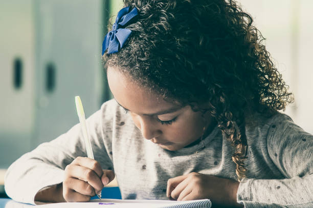 istock Focused curly haired schoolgirl sitting at desk 1296299070