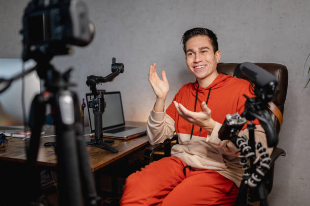 istock Young man sitting at the desk talking to the camera recording a tutorial video. Guy recording a video with professional equipments. 1296299153