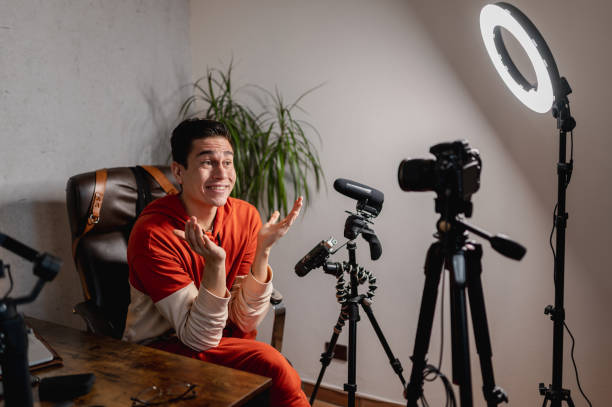 istock Young man sitting at the desk talking to the camera recording a tutorial video. Guy recording a video with professional equipments. 1296299498