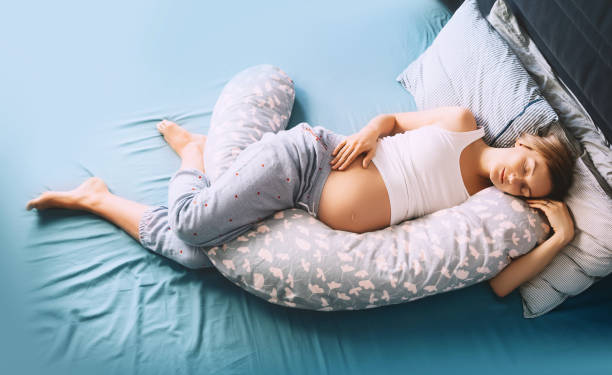 красивая беременная женщина, расслабляющая или спящая с подушкой поддержки живота в постели. молодая мать ждет ребенка. - sleeping women pillow bed стоковые фото и изображения