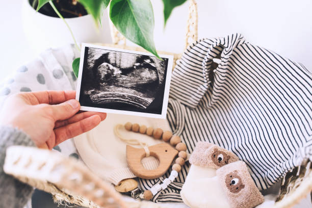 woman's hand holding ultrasound images in background of wicker basket of stuff for newborn baby. - nature human pregnancy color image photography imagens e fotografias de stock