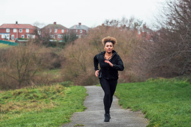 A mid adult mixed race woman wearing casual sporty clothing and running through her local park on a morning in December.