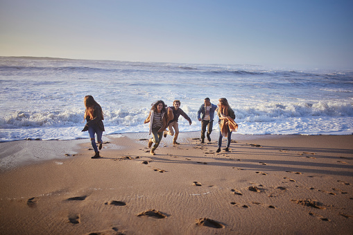 Multi-ethnic friends running from wave at the beach during sunset