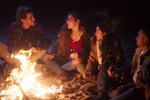 Friends drinking wine bottle at beach bonfire at night Group of young friends drinking wine bottle at beach bonfire at night Bonfire stock pictures, royalty-free photos & images