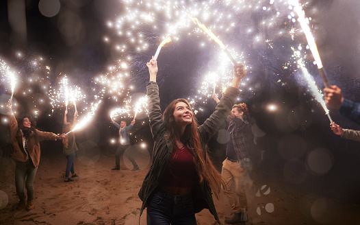 Young friends group playing and having fun with sparklers at the beach at night