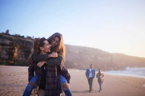 istock Young couple piggyback ride on the beach at sunset 1296316857