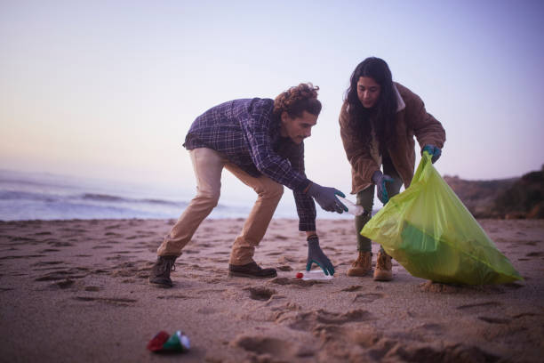 Two friends picking up trash on the beach during sunset
