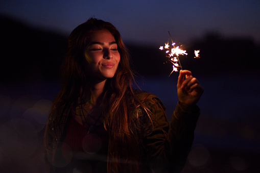 Close-up of young beautiful girl holding sparkler on the beach at night