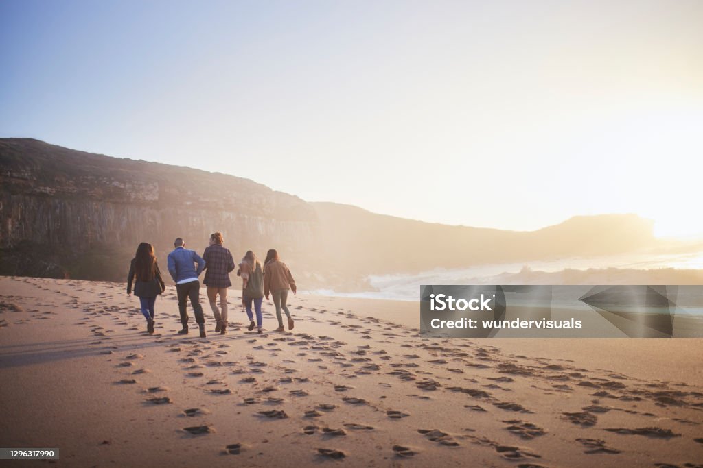 Group of friends walking together on the beach at sunset Back-view of group of friends walking together on the beach at sunset Beach Stock Photo
