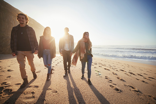 Group of friends silhouette walking together on the beach at sunset