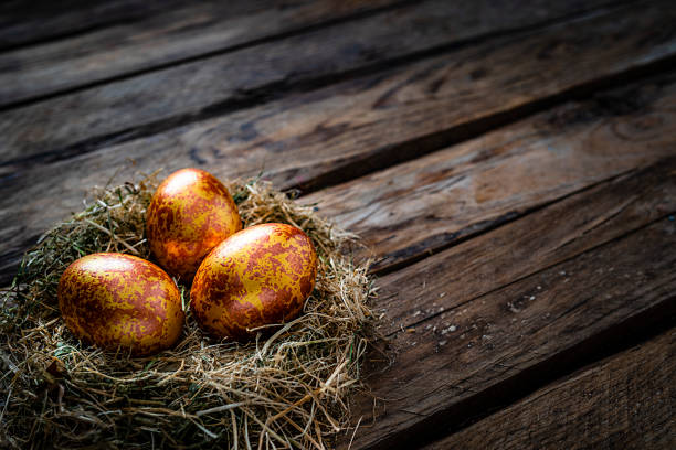 istock Straw nest with three gold colored eggs on rustic wooden table. Copy space 1296318869