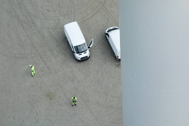 istock Drone view on Professional rope access technician, workers standing under onshore wind-turbine parking lot in Sweden with cars and looking in to the mobile. 1296318871