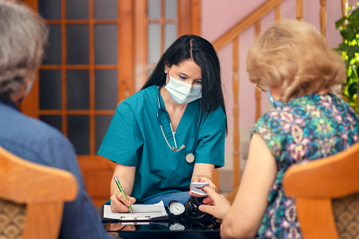 Female nurse doing blood oxygen measurement with pulse oximeter to senior people during home visit – Doctor or caregiver with face mask doing coronavirus test by checking health of elderly patients