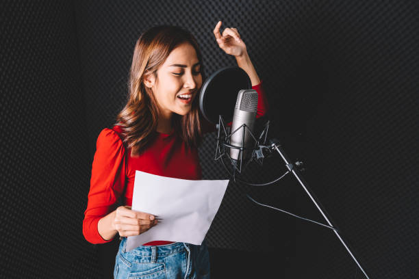 istock Pretty Asian female singer recording songs by using a studio microphone and pop shield on mic with passion in music recording studio. Performance and show in the music business. Image with copy space. 1296320250
