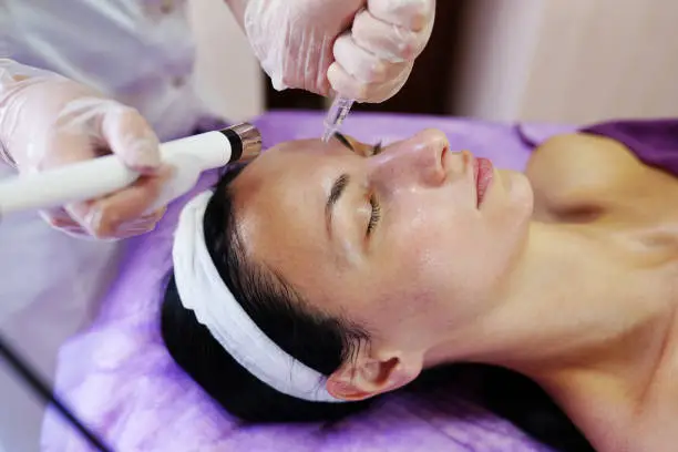 Photo of Microcurrent facial massage. Beautician in white gloves holding the electrode of the massage apparatus and syringe. Hardware cosmetology.