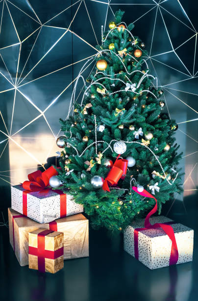 istock Decorated Christmas tree and wrapping gift boxes near wall background. Festive decorating green tree and Santa presents, xmas modern home decor 1296322466