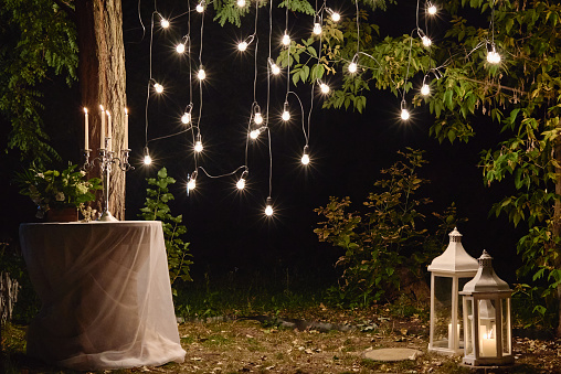 Night wedding ceremony with candles, lanterns and bulb lights on tree outdoors, copy space