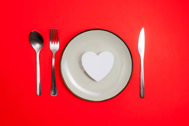 istock Romantic valentines day dinner idea concept. Heart on plate and silver wear on red background. 1296328221