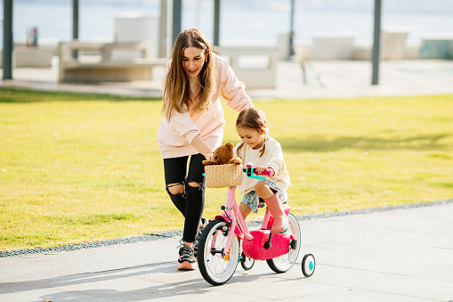 Photo of a young girl and his mother on a bicycle lane, learning to ride a bike.