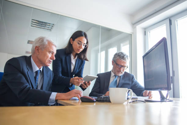istock Young pretty secretary showing data on tablet to senior managers 1296332387