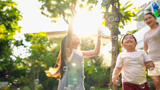 padres con dos hijos jugando burbujas de jabón juntos en el jardín del patio trasero. - park child asia lifestyles fotografías e imágenes de stock