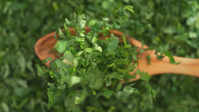 Chopped Parsley on Olive Wood Spoon in Macro Falling onto Green Herbs and Slow Motion