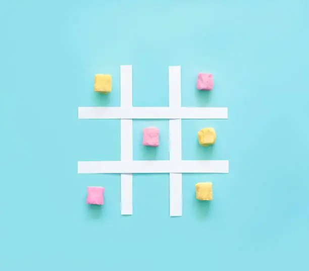 Tic tac toe made of pink and yellow marshmallows on a blue background.