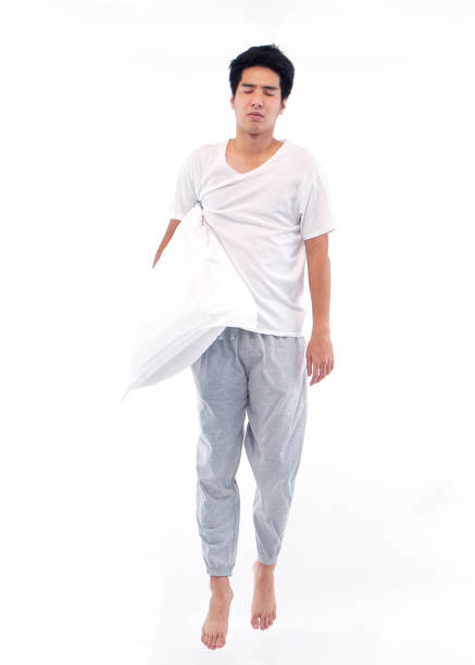 istock Young man in pajamas embracing pillow on white background 1296339633
