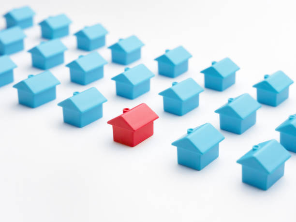 istock Unique house different from group of same type miniature houses. Red house model among blue toy houses on white color background. Home choice or selection property and real estate. Property marketing 1296339770