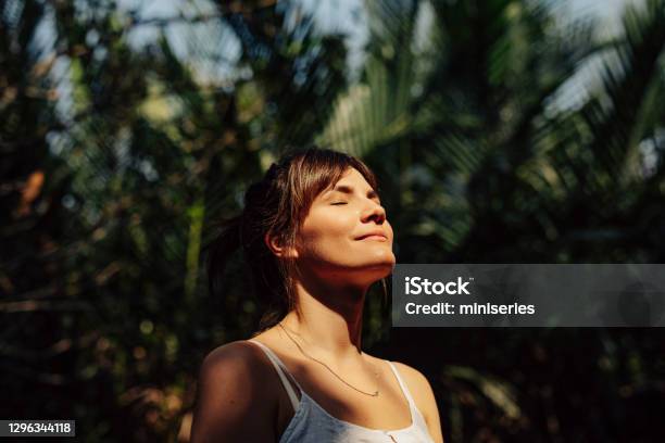 Hermosa Mujer Feliz Disfrutando De La Cálida Luz Del Sol En Un Parque Público Tropical Foto de stock y más banco de imágenes de Mujeres