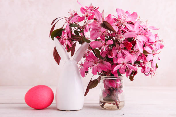 statuina di coniglietto pasquale accanto a uova dipinte e bouquet di fiori rosa - easter egg figurine easter holiday foto e immagini stock