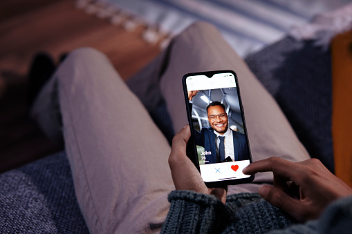 Midsection of man using dating app mobile on phone displaying handsome gay man while sitting on sofa at home