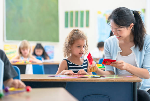 Good job recognizing the alphabets! A mixed race preschool girl is getting some help from her teacher who is next to her desk with some flash cards exercise. literacy photos stock pictures, royalty-free photos & images