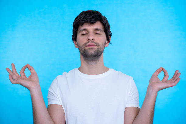 istock Young male keeping eyes closed while practicing yoga indoors, meditating, holding hands in mudra gesture 1296352628