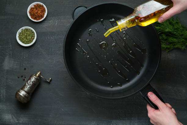 человек наливая растительное масло на сковороде - вид сверху на темном фоне - cooking oil oil pouring olive oil стоковые фото и изображения