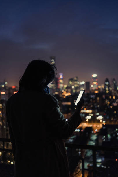 istock Woman Using Smartphone on Skyscraper Roof at Night 1296356684