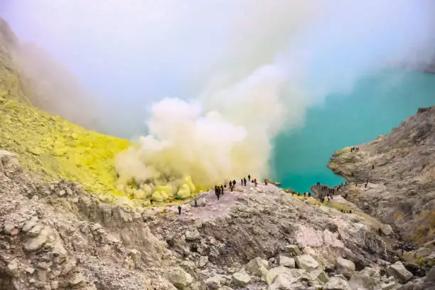 Photo of Crater of a volcano with a green sulfuric volcanic lake and volcanic smoke. View of the smoking volcano Kawah Ijen in Indonesia. Mountain landscape Extracting Sulphur inside Kawah Ijen crater