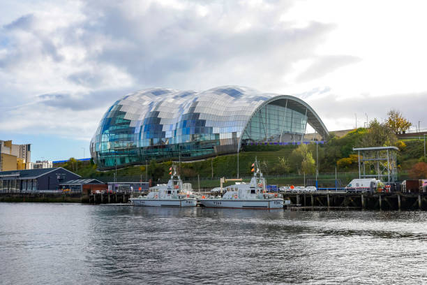 The Sage Gateshead viewed from Newcastle quayside.  There are navy vessels parked alongside a military recruitment centre in early morning light. Gateshead, Tyne and Wear, England, UK.