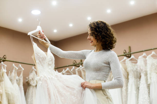 jeune femme regardant une robe de mariée dans une boutique de mariage - robe de mariée photos et images de collection