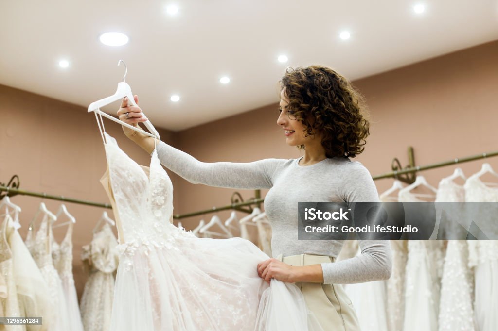 Young woman looking at a wedding dress in a bridal shop Young woman choosing a wedding dress in a bridal shop. About 25 years old, Caucasian brunette. Wedding Dress Stock Photo