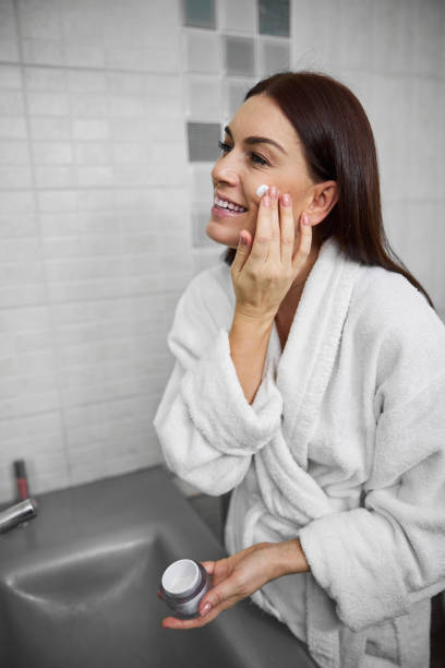 istock Cheerful pretty female applying face cream at home 1296361453