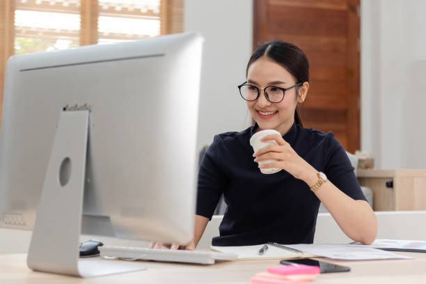 istock Work from home concept, a happy smiling beautiful Asian women Working at desktop computer hold a coffee cup It is a new normal lifestyle of the online era. 1296363499