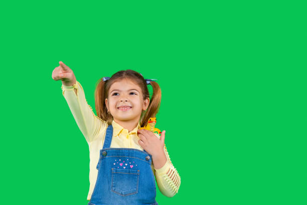 istock A preschool girl holds a lizard on her shoulder and points forward with her forefinger. Green background with side space 1296365936