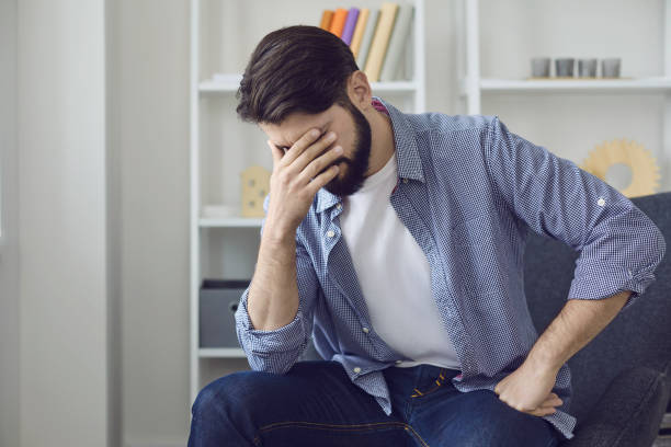 istock Sad man sitting at home, feeling bad and touching face with hand 1296368906