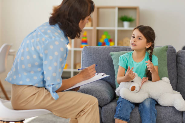 Happy little girl telling story to child psychologist during therapy session in cozy modern office stock photo