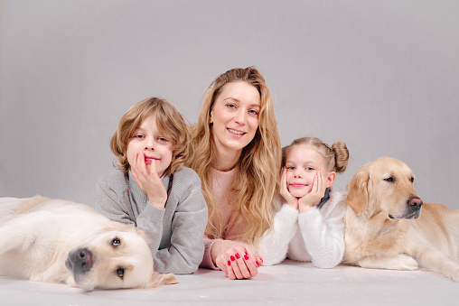 Mom with her son and daughter lie on the floor with two large dogs on a white background. The family plays with the dogs. The concept of love and care and pet animals.