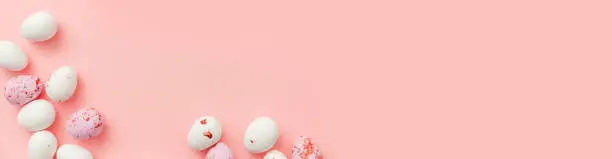 Happy Easter concept. Preparation for holiday. Easter candy chocolate eggs and jellybean sweets isolated on trendy pastel pink background. Simple minimalism flat lay top view copy space banner